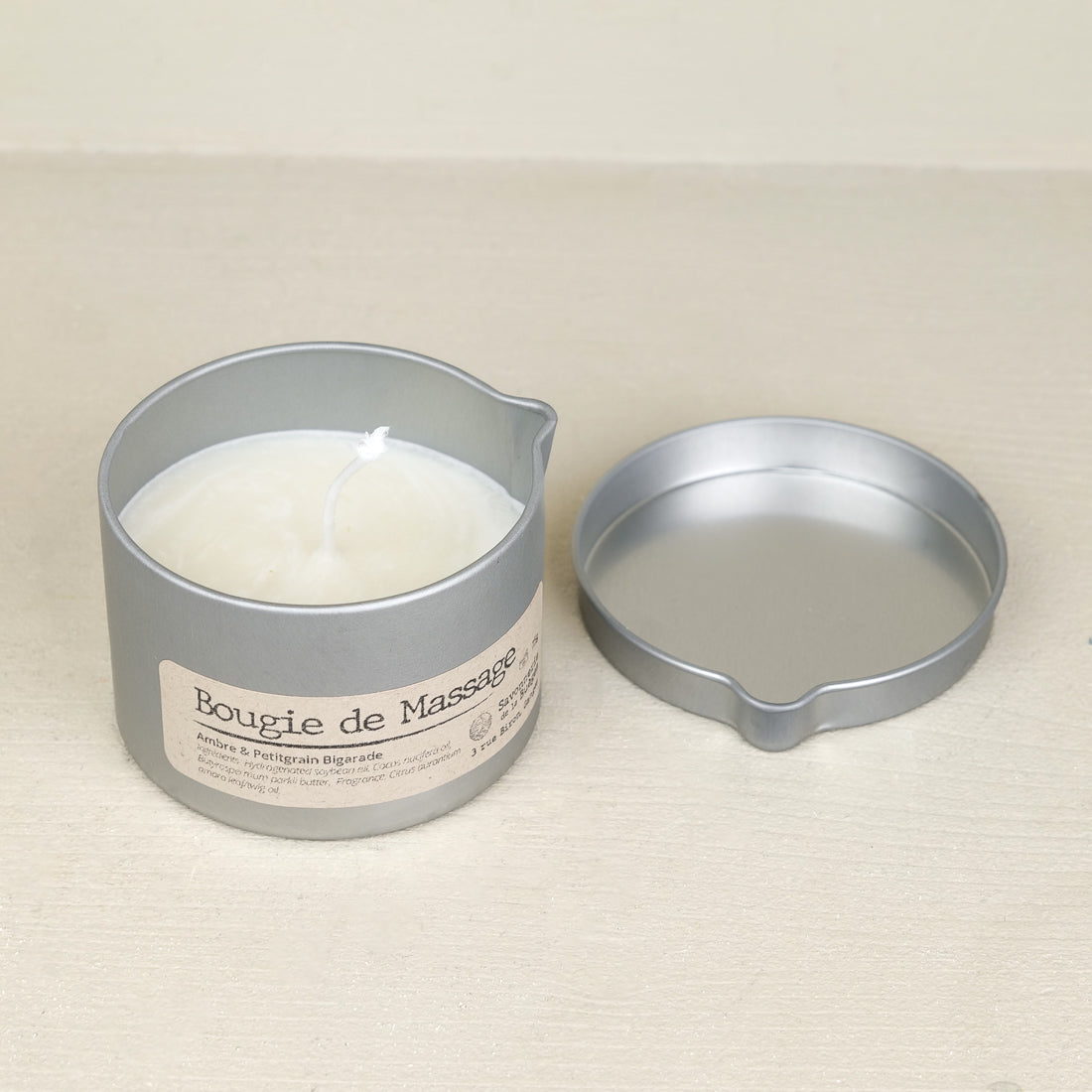Organic soy wax massage candle with shea butter in a 75 g metal tin, lid removed and set beside it