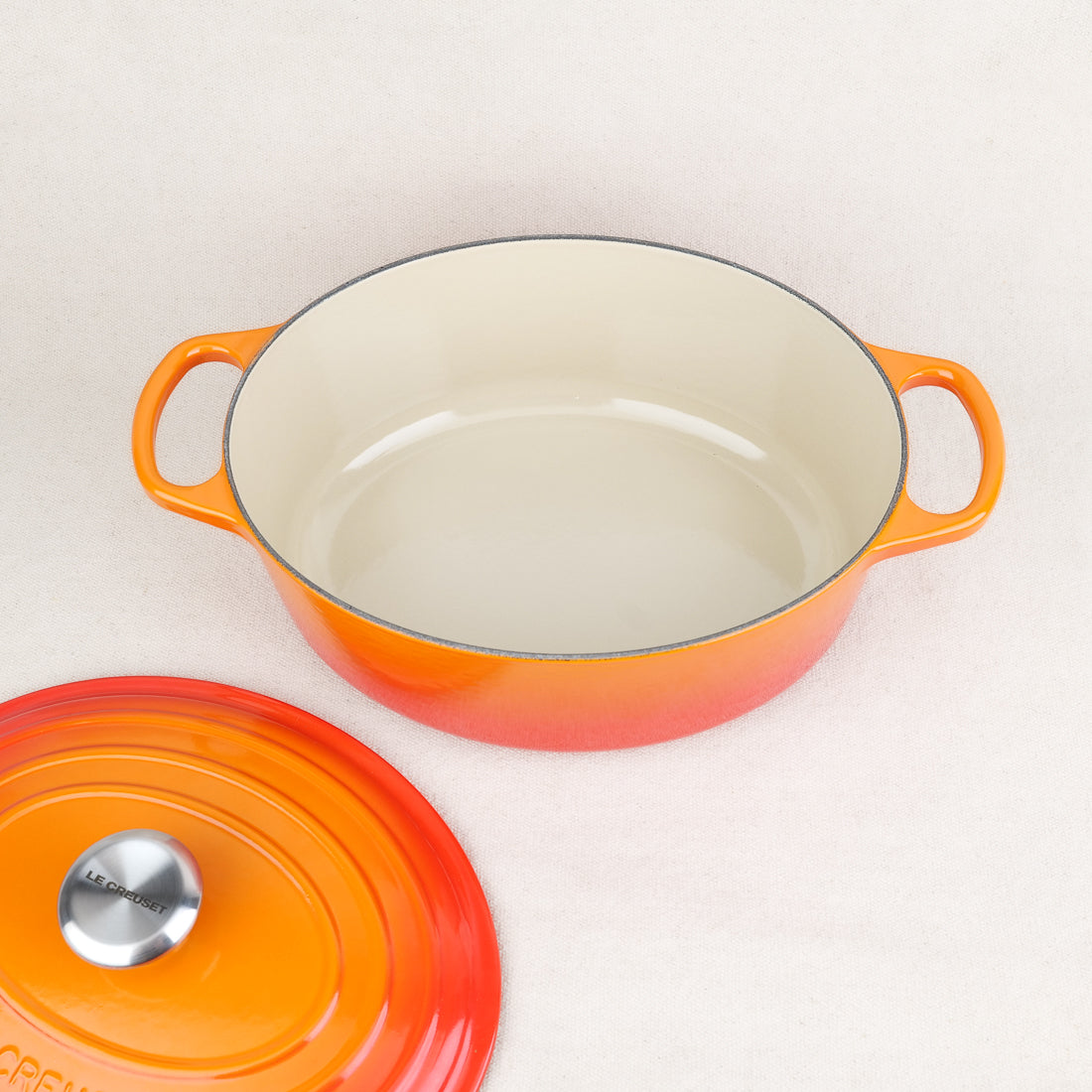 Intérieur émaillé crème d'une cocotte ovale Le Creuset Volcanique en fonte, couvercle posé à côté, fabrication française