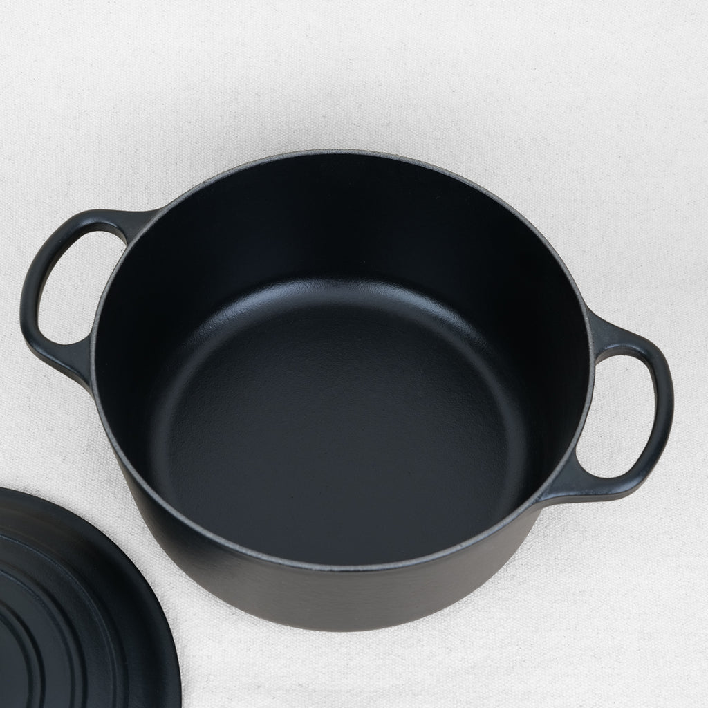 Intérieur de cocotte ronde Le Creuset en fonte émaillée noir mat, fabrication française, couvercle posé à côté