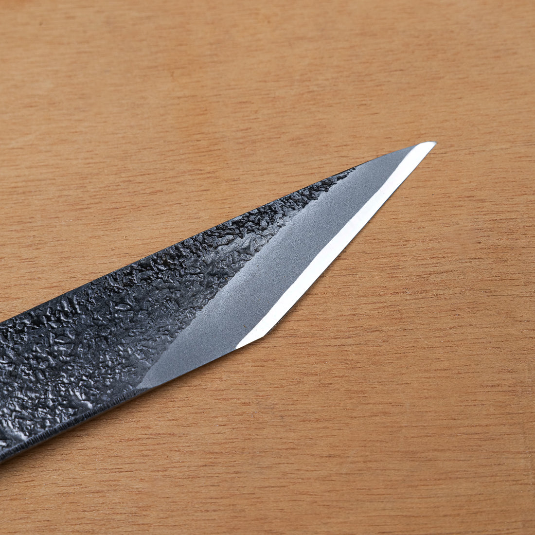 Gros plan sur le tranchant biseauté et la surface martelée Tsuchime du couteau de marquage kiridashi en acier forgé Takagi