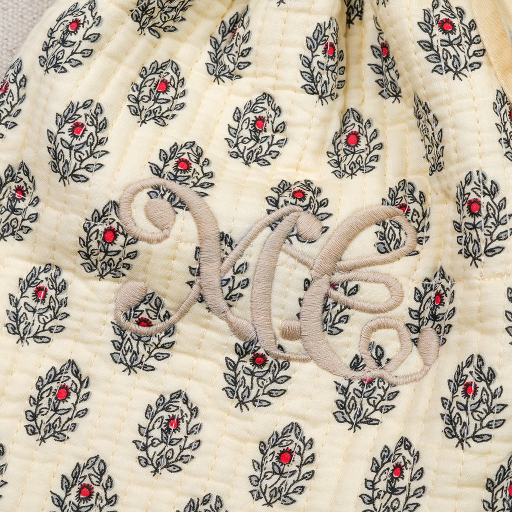 Gros plan sur le monogramme brodé beige d'une housse de bouillotte provençale Empereur en coton matelassé crème