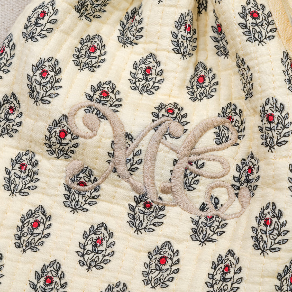 Gros plan sur le monogramme brodé beige d'une housse de bouillotte provençale Empereur en coton matelassé crème