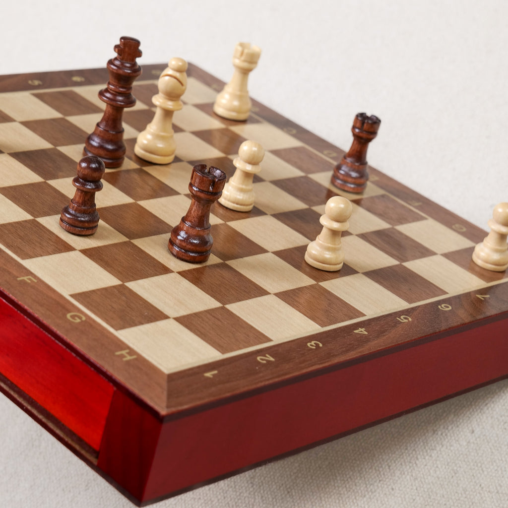 Pièces d'échecs en bois bicolores disposées sur l'échiquier magnétique Goki 56919, coffret 25x25 cm avec tiroirs laqués rouge