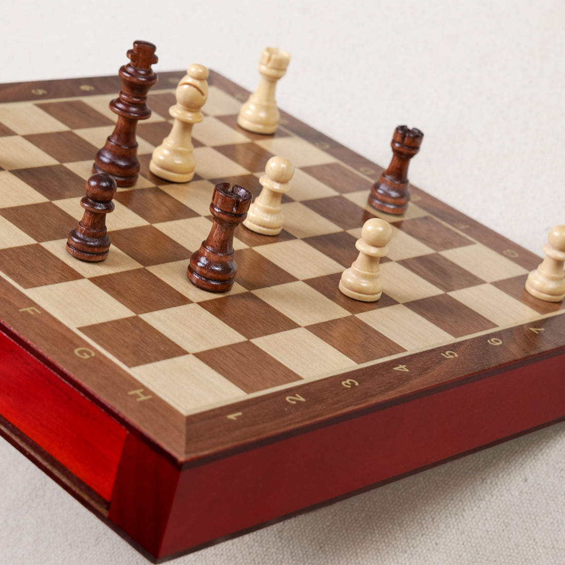 Pièces d'échecs en bois bicolores disposées sur l'échiquier magnétique Goki 56919, coffret 25x25 cm avec tiroirs laqués rouge