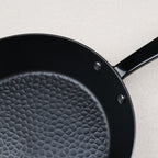 Gros plan sur le fond martelé d'une poêle en acier nitruré compatible induction, manche fixé par rivets inox