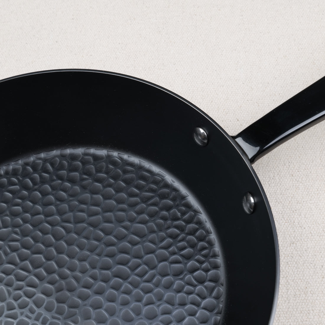 Gros plan sur le fond martelé d'une poêle en acier nitruré compatible induction, manche fixé par rivets inox
