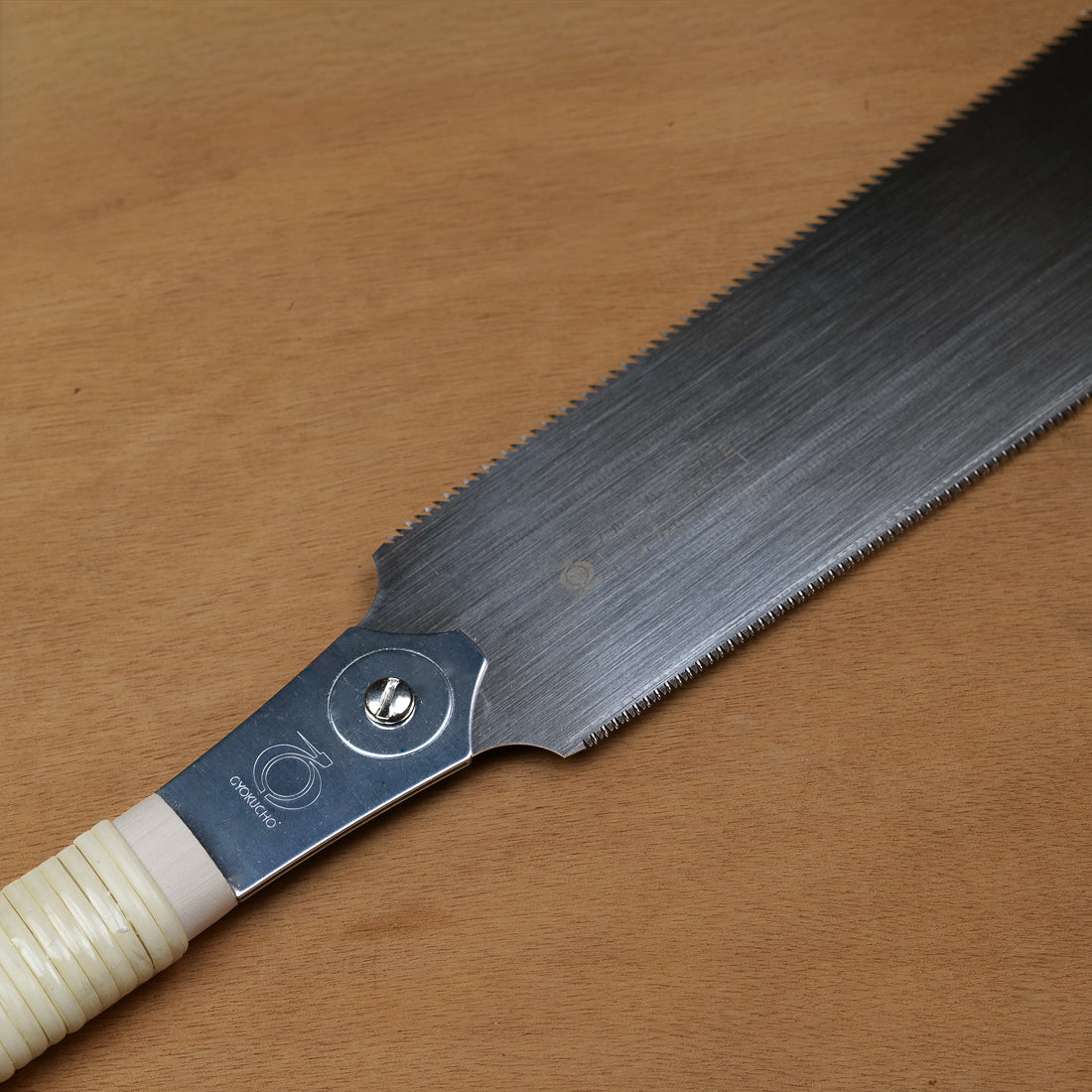 Gros plan sur la lame fine et le manche en rotin de la scie de menuisier Ryoba Komame, fabrication japonaise